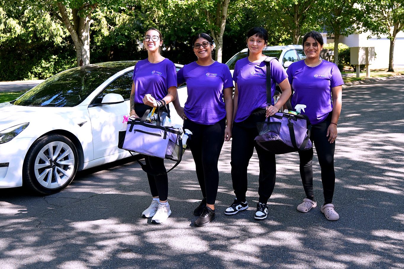 Four members of the Tuane's Cleaning team in purple uniforms, carrying their cleaning bags